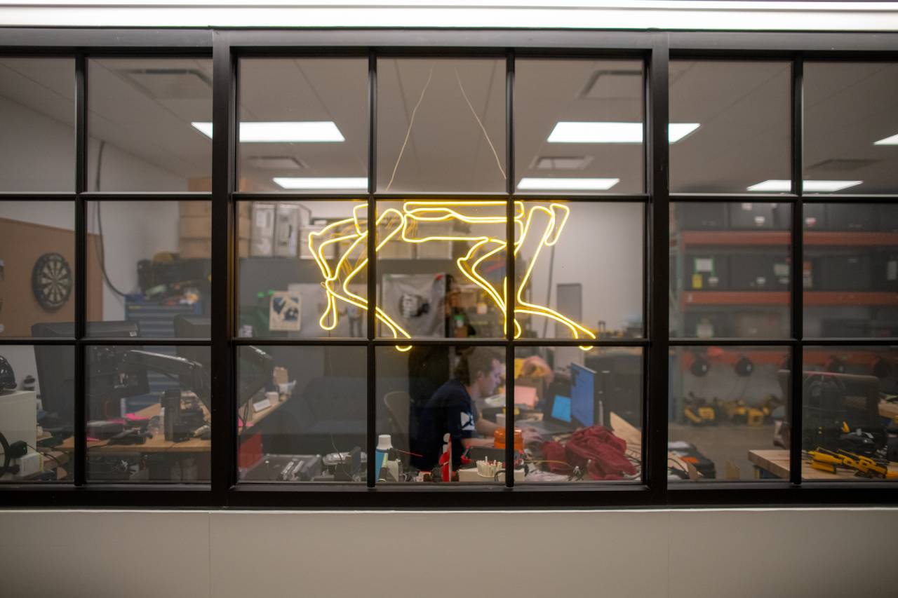 Employees work behind a window displaying a neon sign shaped like Spot