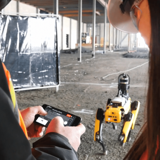 two operators on a construction site drive spot from a cell phone