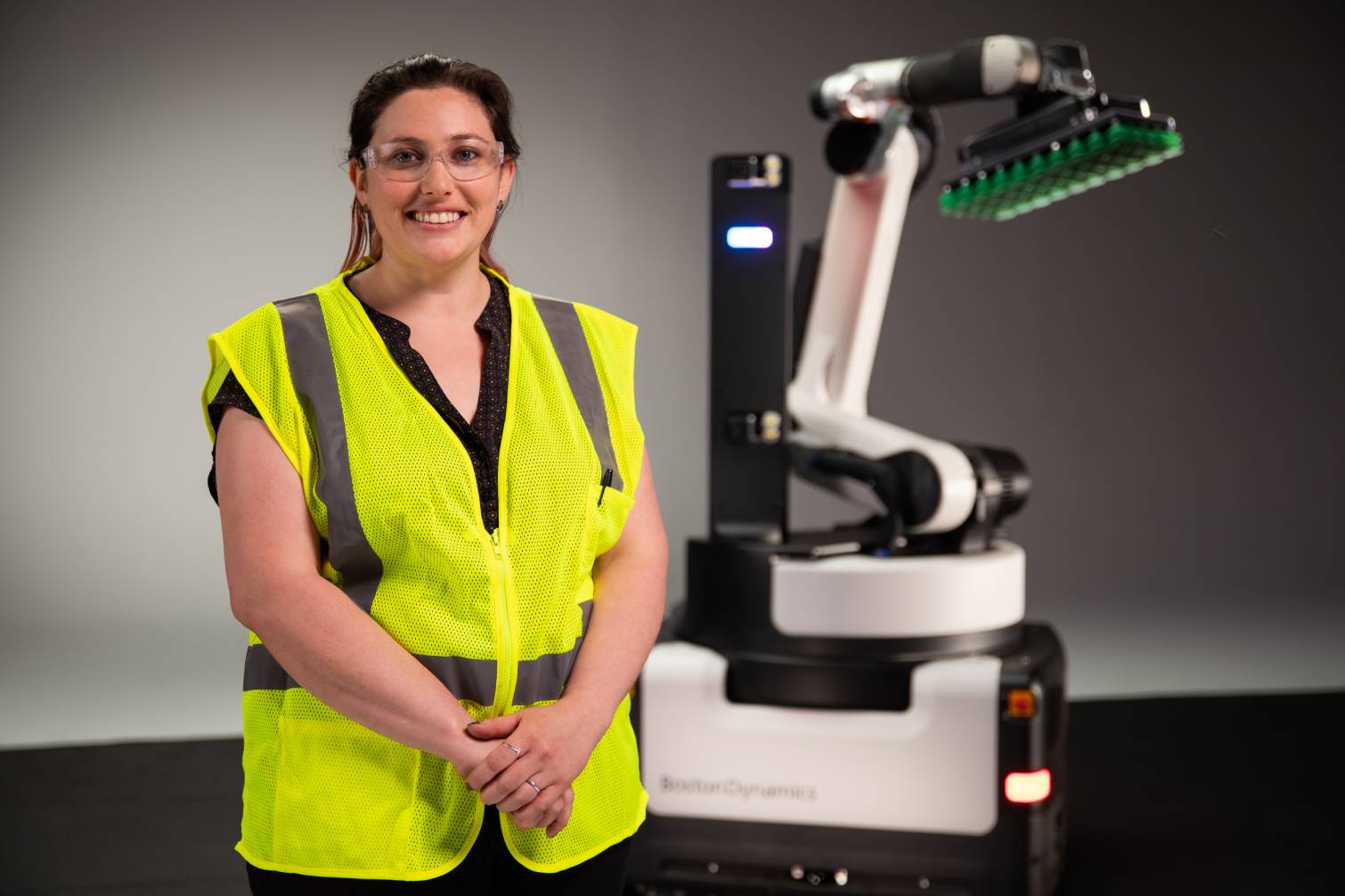 A worker wearing protective gear and standing with the Boston Dynamics Stretch robot