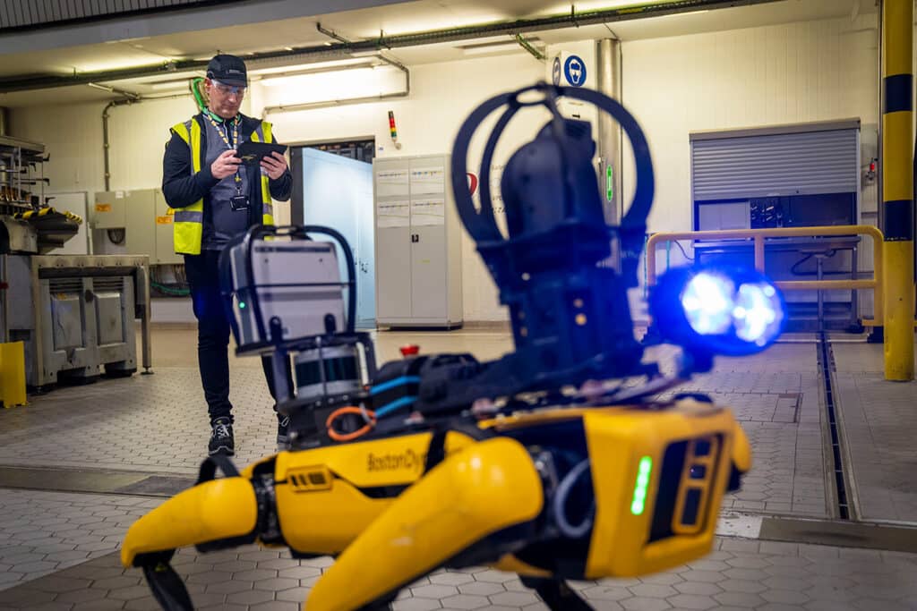 An operator stands behind Spot, setting up an autonomous inspection route on the Spot tablet controller