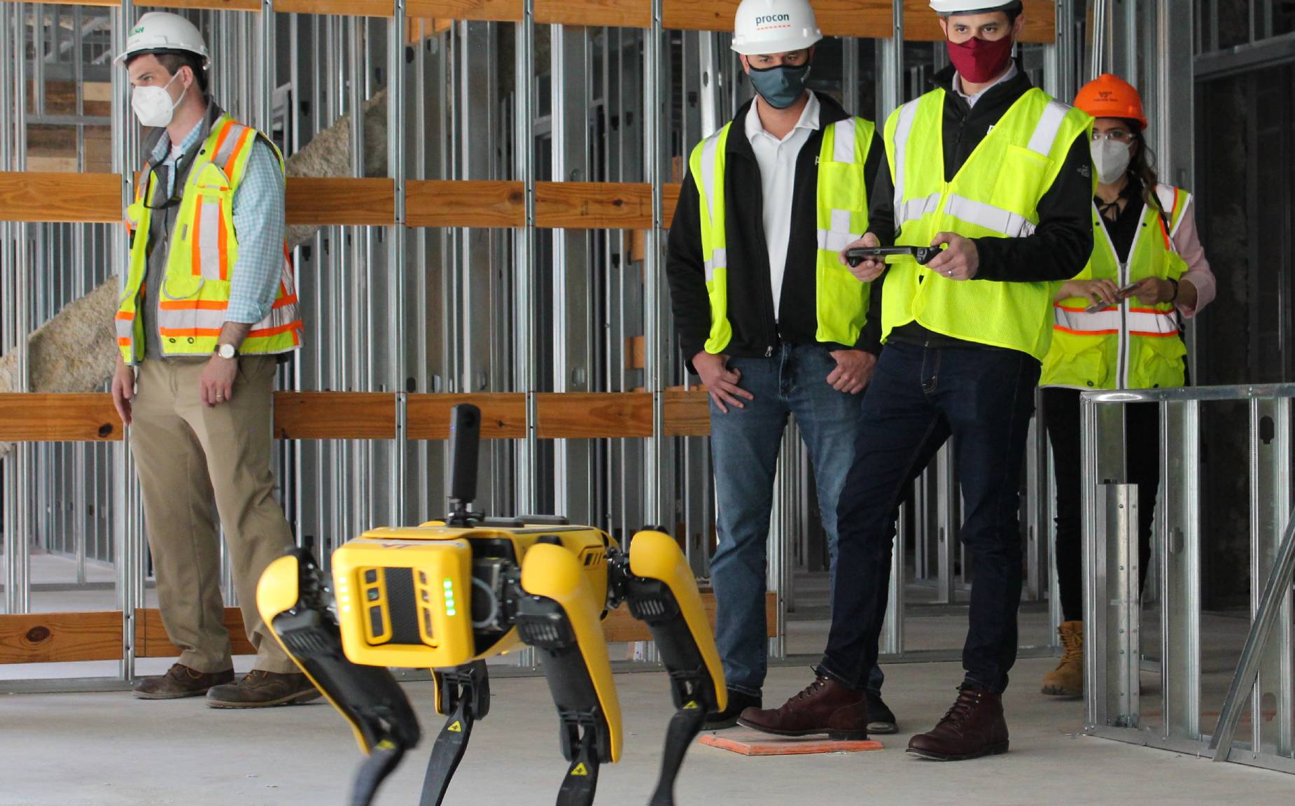 Masked construction workers operating Spot on a jobsite