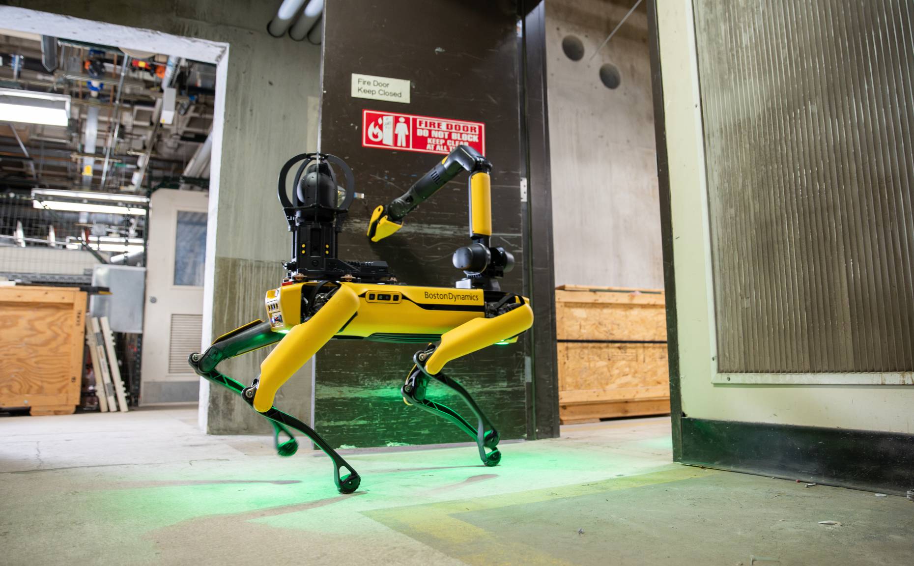 Spot using its arm to move through a doorway in an industrial facility