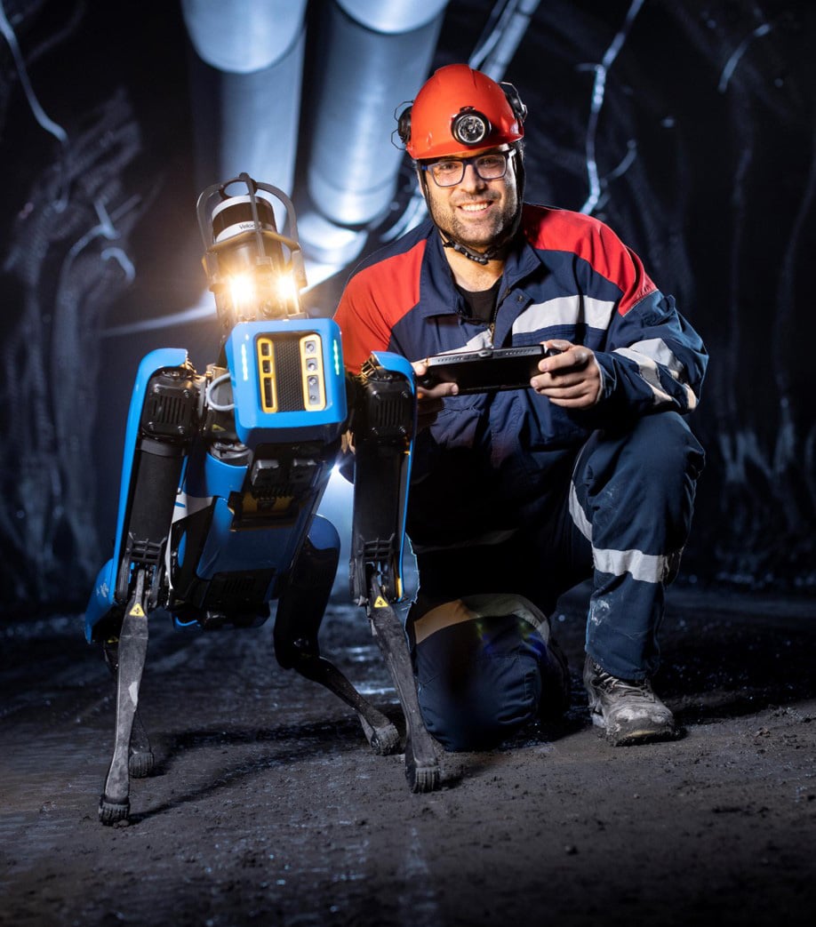 an operator in a hardhat poses with Spot in a mine tunnel